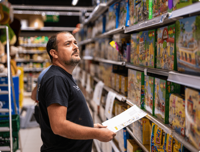 Man in zwart T-shirt met een document kijkt naar speelgoeddozen in een winkelschap