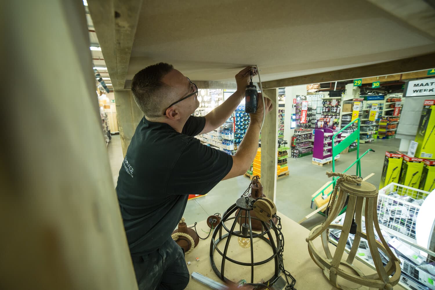 Technicus boort in het plafond van een houten opstelling om lampen te monteren in een doe-het-zelfzaak