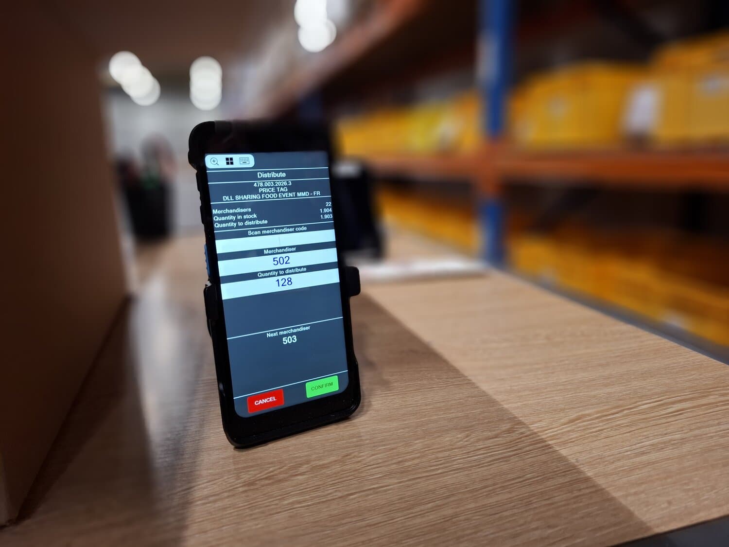 Handheld scanner showing a Distribute screen on a wooden shelf in front of warehouse racking