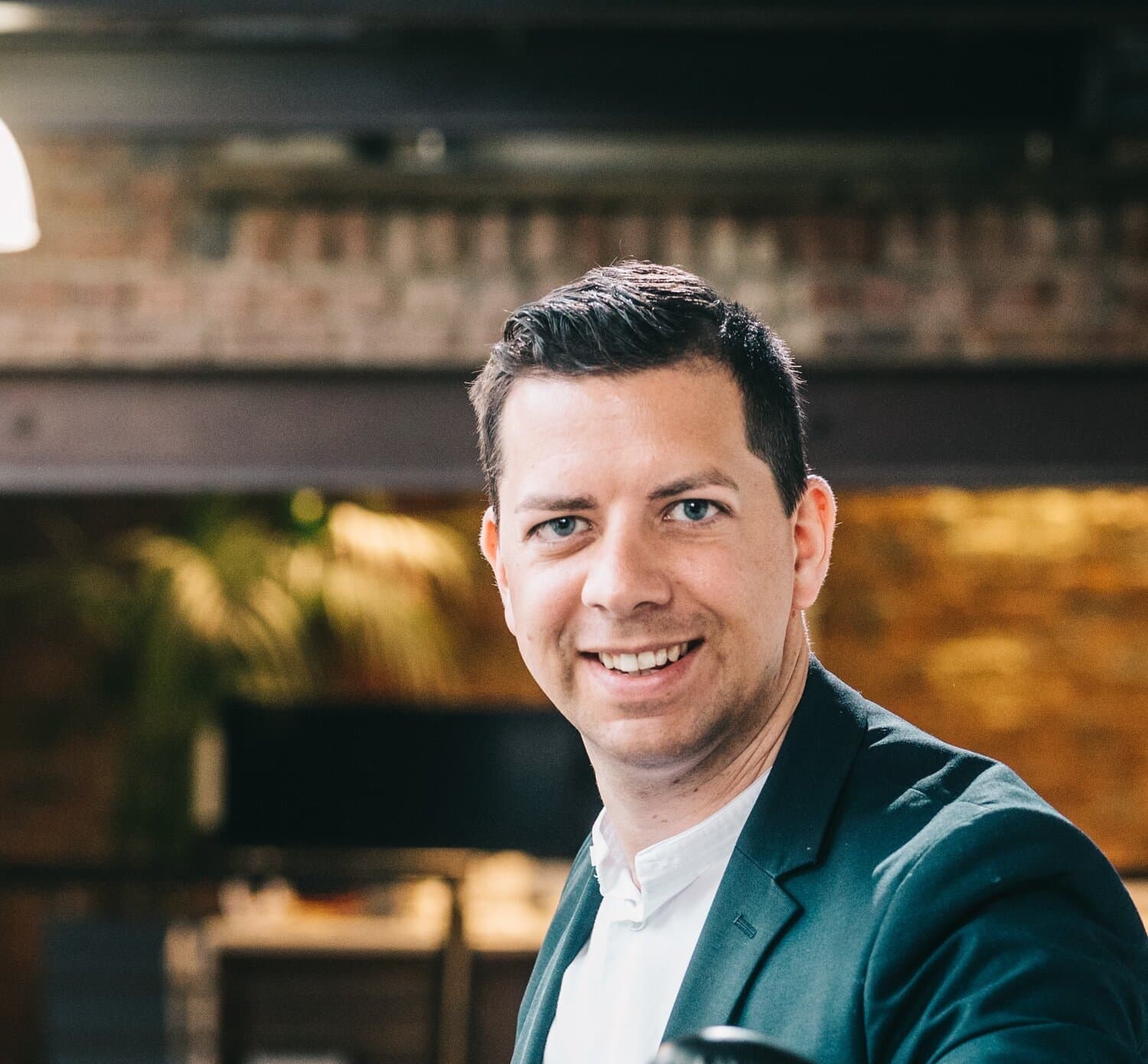 Dave Froidcoeur of Carrefour Belgium smiling, wearing a dark blazer and white shirt in front of a brick wall