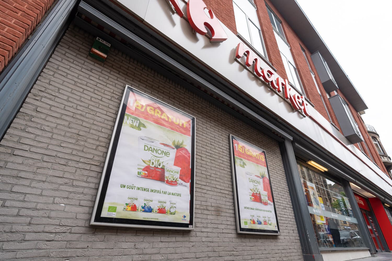 Two Danone Bio posters on the exterior brick wall of a Carrefour Market store