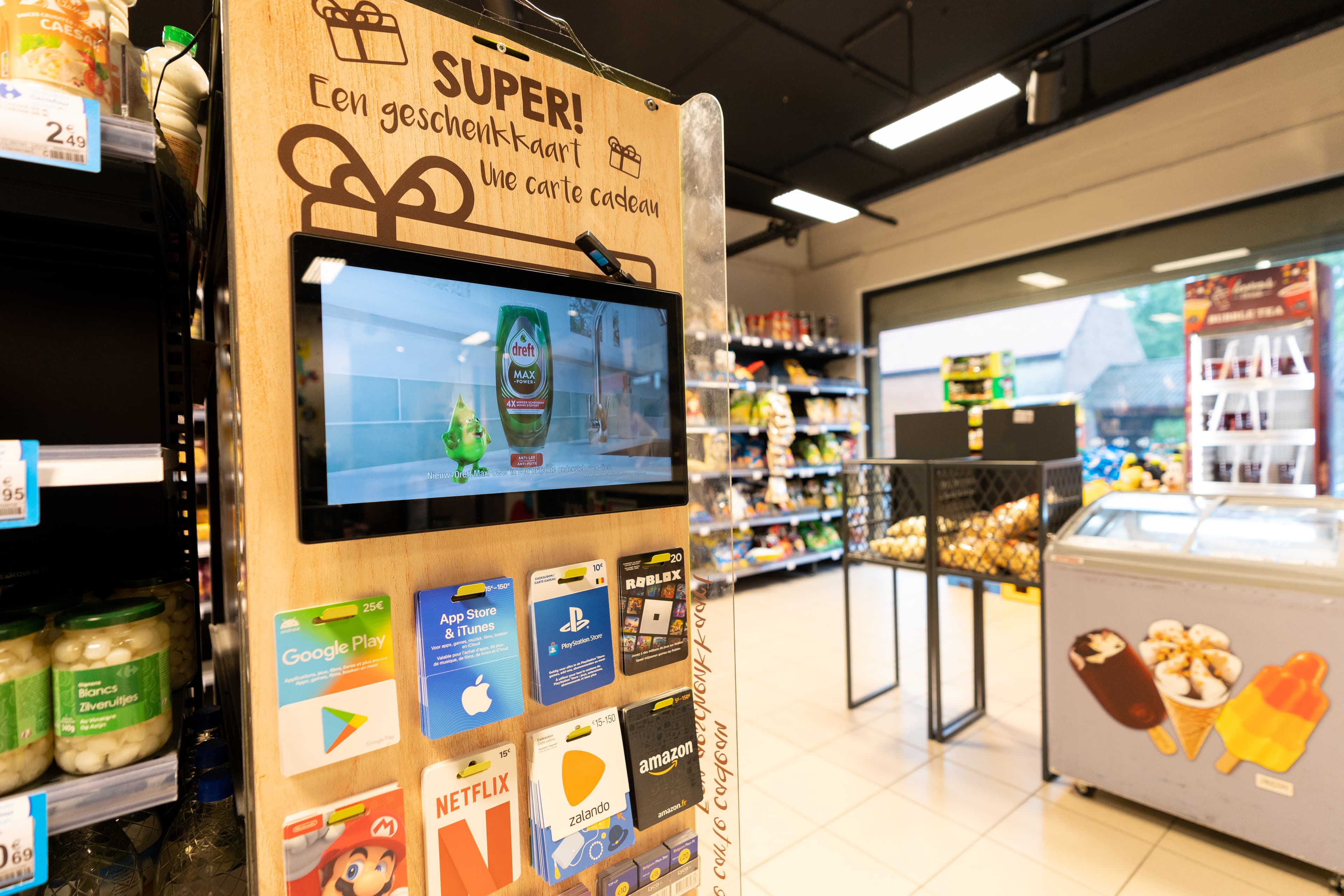 Wooden display with screen showing a Dreft ad and gift cards in a Carrefour supermarket