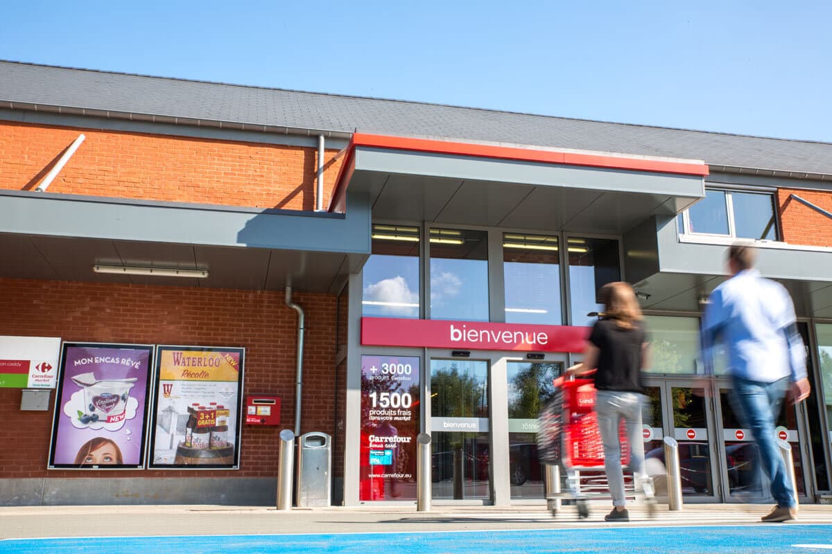 Carrefour Market supermarket entrance with two advertising posters on the brick wall and two blurred shoppers in front