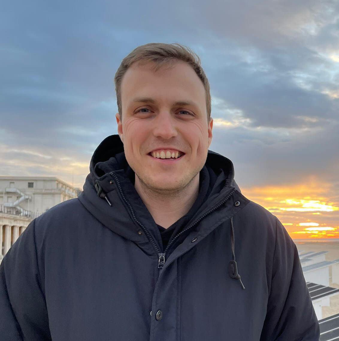 Marnik Meskens souriant en veste à capuche, coucher de soleil sur la plage