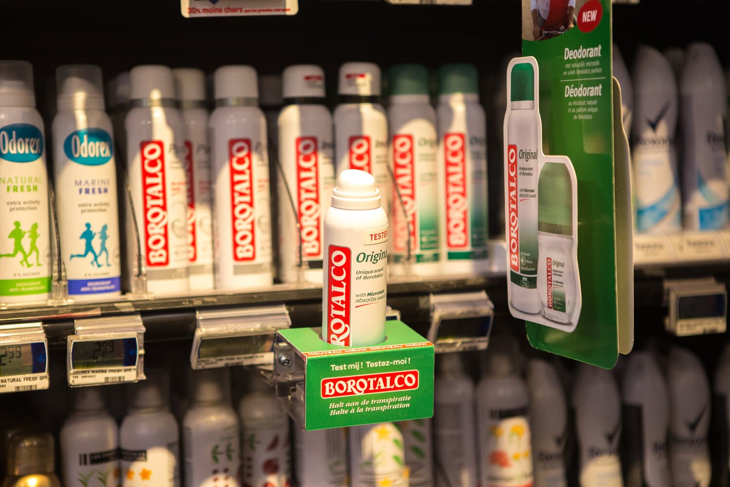 Borotalco deodorant tester in a green holder on a shelf among Odorex and Rexona sprays