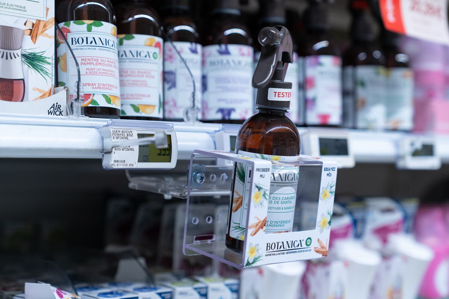 Botanica room spray tester bottle in a clear holder on a store shelf beside electronic price labels