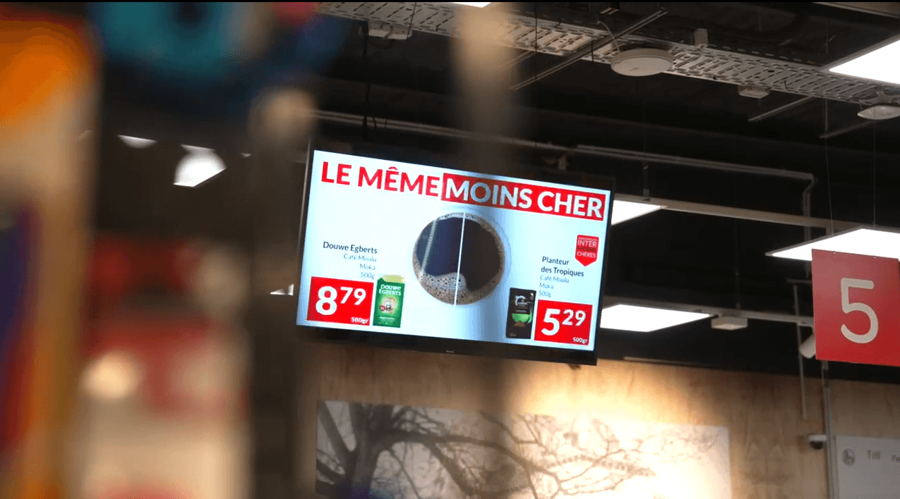 Hangend scherm in de winkel vergelijkt twee koffies: Douwe Egberts aan 8,79 en Planteur des Tropiques aan 5,29