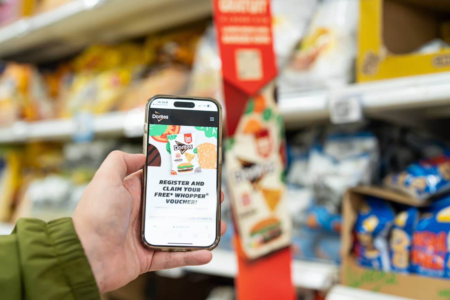 Hand holding a smartphone showing the Doritos website in front of a snack shelf with a red shelf display