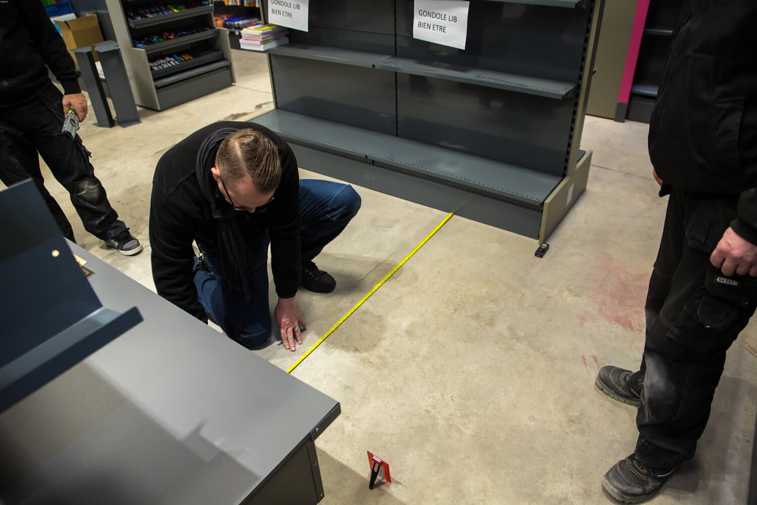 Een technicus hurkt om de vloer te meten met een rolmeter bij lege schappen in een winkel