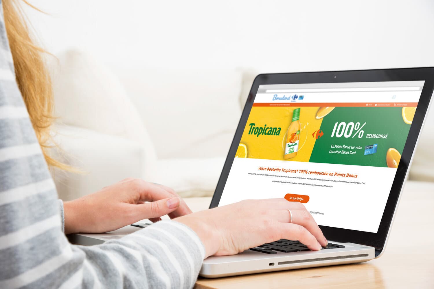 Femme tapant sur un ordinateur portable affichant une offre Tropicana 100% remboursé en Points Bonus Carrefour